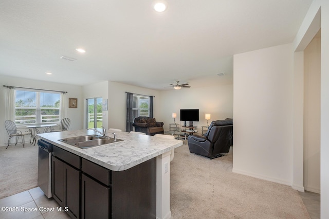 kitchen with sink, dark brown cabinets, an island with sink, light carpet, and stainless steel dishwasher