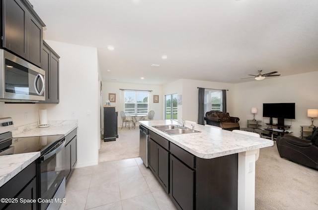 kitchen with appliances with stainless steel finishes, sink, ceiling fan, light carpet, and a center island with sink