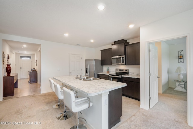 kitchen with stainless steel appliances, sink, a kitchen island with sink, and light carpet