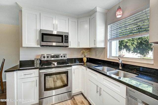 kitchen featuring sink, white cabinets, dark stone counters, stainless steel appliances, and light hardwood / wood-style flooring