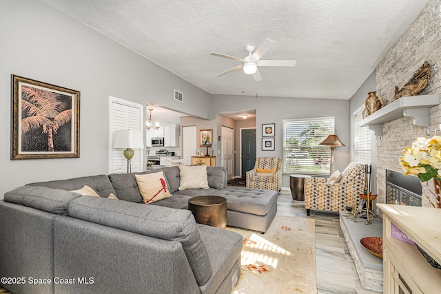 living room with lofted ceiling, light hardwood / wood-style flooring, a textured ceiling, ceiling fan, and a fireplace