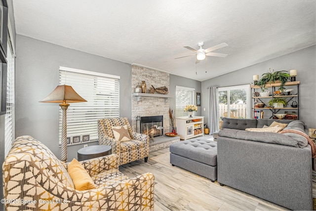 living room with a stone fireplace, lofted ceiling, ceiling fan, a textured ceiling, and light hardwood / wood-style flooring