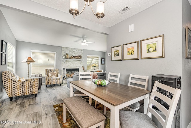 dining room with a fireplace, light hardwood / wood-style floors, ceiling fan with notable chandelier, and a textured ceiling