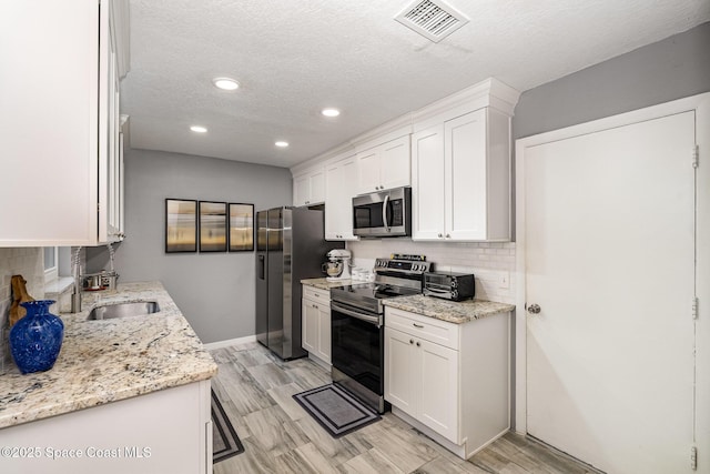 kitchen featuring stainless steel appliances, light stone countertops, and white cabinets