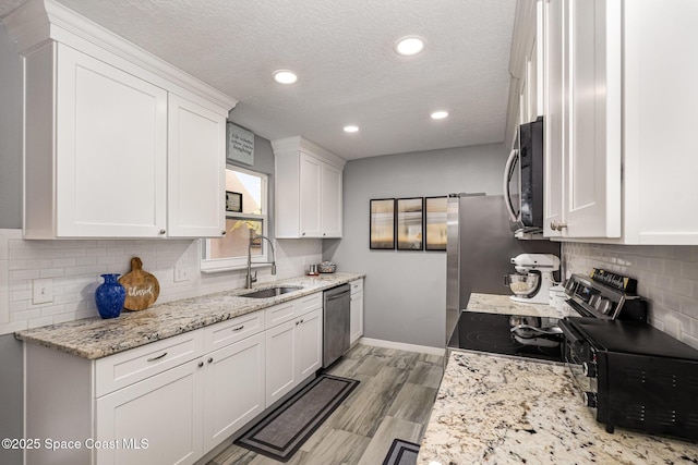 kitchen featuring sink, white cabinetry, stainless steel appliances, light hardwood / wood-style floors, and light stone countertops