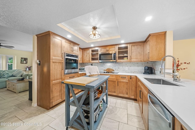 kitchen with sink, a tray ceiling, decorative backsplash, and appliances with stainless steel finishes