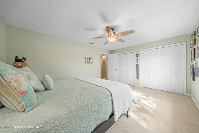 bedroom with ceiling fan, a textured ceiling, carpet floors, and multiple closets