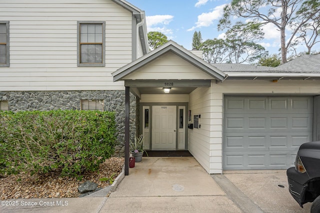 entrance to property featuring a garage, driveway, and roof with shingles