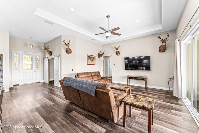 living room featuring ceiling fan, hardwood / wood-style flooring, a barn door, and a raised ceiling