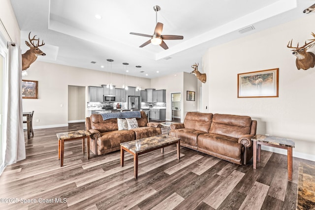 living room with a raised ceiling, dark hardwood / wood-style floors, and ceiling fan