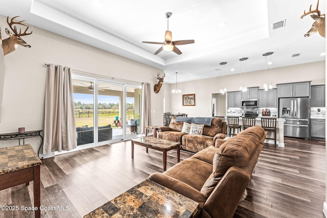 living room featuring a raised ceiling, dark wood-type flooring, and ceiling fan