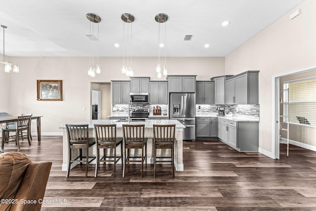 kitchen with decorative light fixtures, appliances with stainless steel finishes, a kitchen breakfast bar, gray cabinets, and backsplash