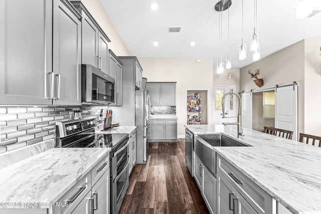 kitchen with a kitchen bar, sink, hanging light fixtures, appliances with stainless steel finishes, and a barn door