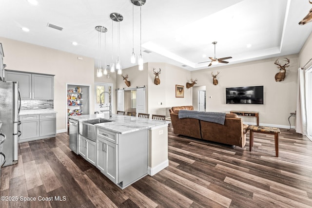 kitchen with a kitchen island with sink, a barn door, a raised ceiling, and appliances with stainless steel finishes