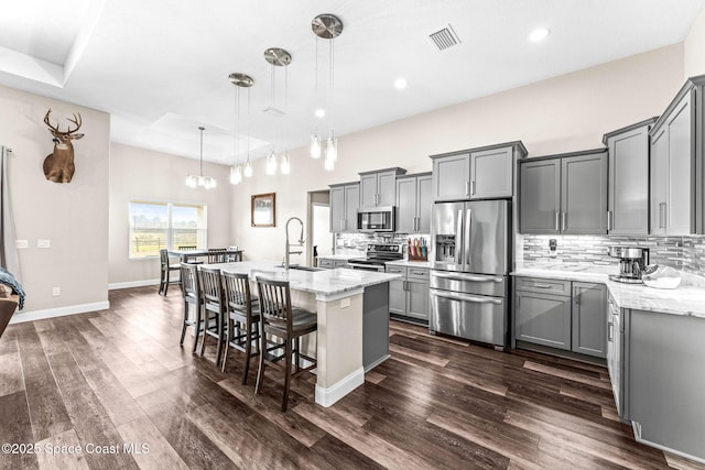 kitchen with stainless steel appliances, a kitchen island with sink, pendant lighting, and gray cabinetry