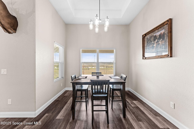 dining room featuring a notable chandelier, dark hardwood / wood-style flooring, a raised ceiling, and a wealth of natural light