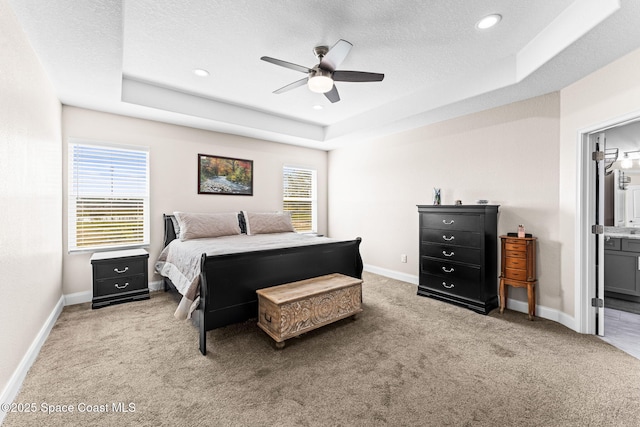 carpeted bedroom with a raised ceiling, connected bathroom, and a textured ceiling