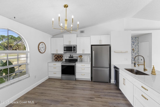 kitchen with sink, vaulted ceiling, pendant lighting, stainless steel appliances, and white cabinets