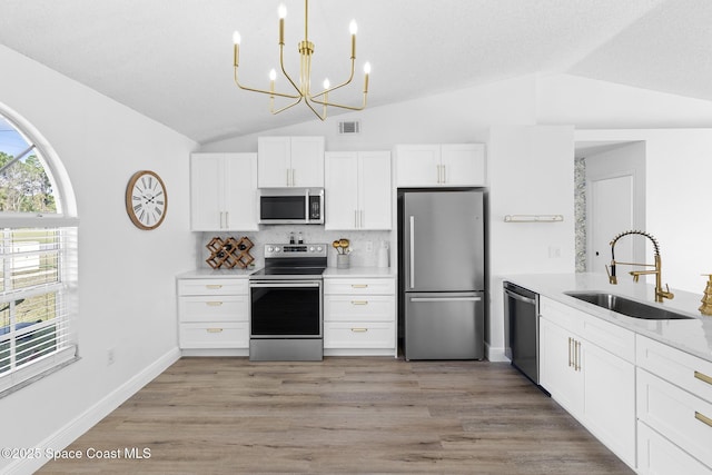 kitchen with vaulted ceiling, appliances with stainless steel finishes, pendant lighting, white cabinetry, and sink