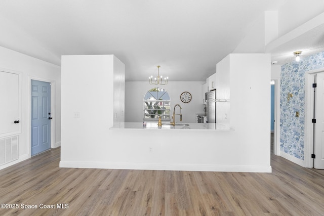 kitchen with stainless steel refrigerator, sink, white cabinets, an inviting chandelier, and light hardwood / wood-style flooring