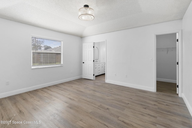 unfurnished bedroom featuring ensuite bathroom, a spacious closet, vaulted ceiling, a textured ceiling, and hardwood / wood-style flooring