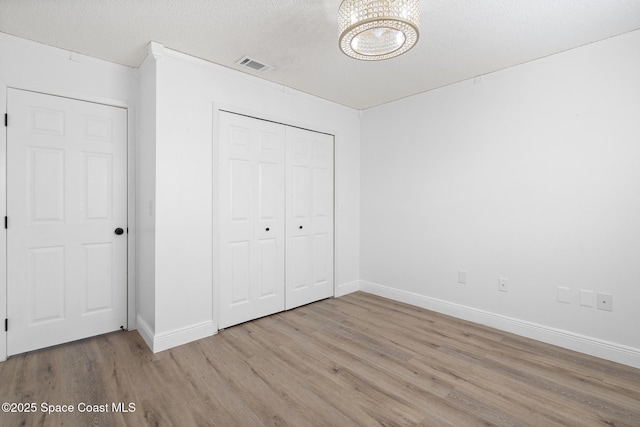 unfurnished bedroom with a textured ceiling, light wood-type flooring, and a closet