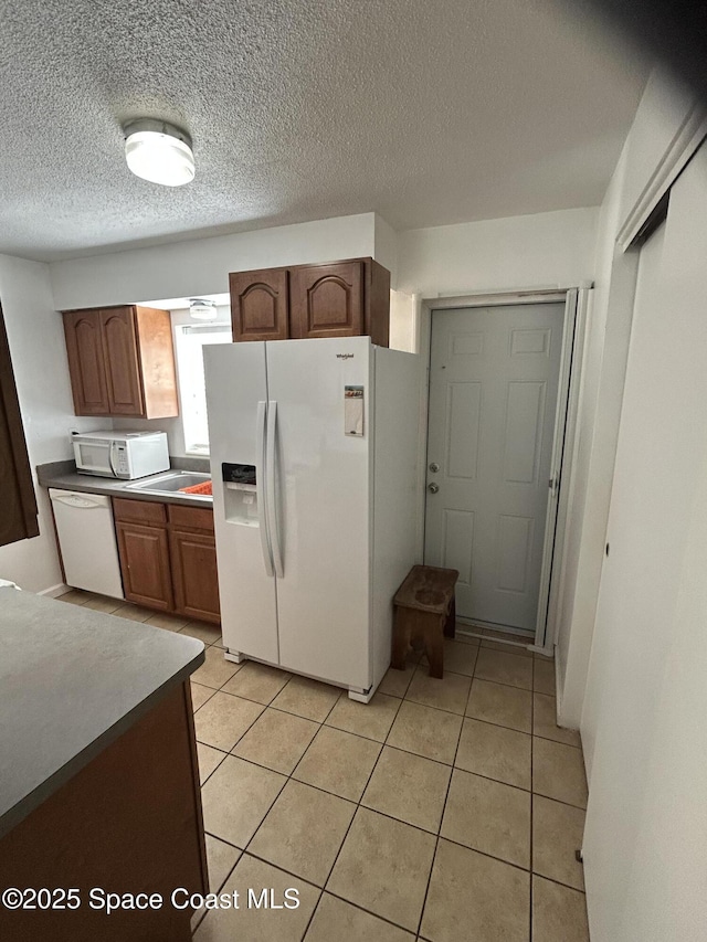 kitchen with light tile patterned floors, a textured ceiling, and white appliances