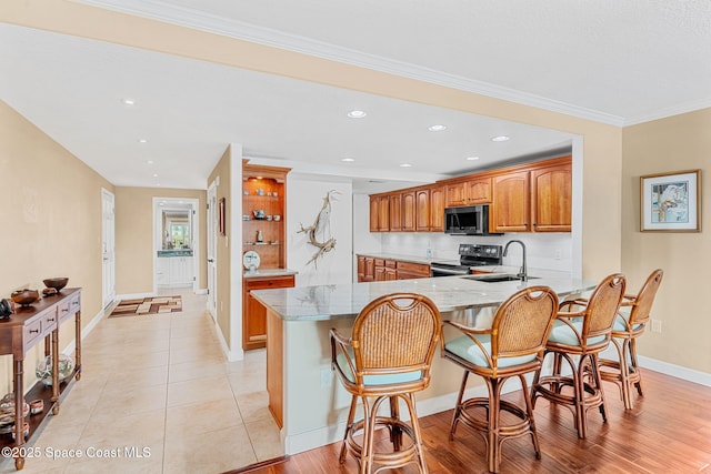 kitchen featuring sink, a kitchen breakfast bar, light stone counters, range with electric stovetop, and kitchen peninsula