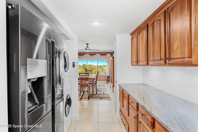 kitchen featuring stainless steel refrigerator with ice dispenser, stacked washer and clothes dryer, light tile patterned floors, light stone countertops, and backsplash