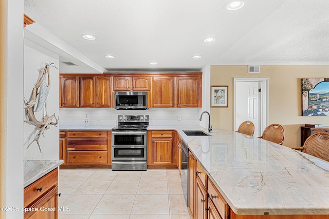 kitchen with sink, light tile patterned floors, appliances with stainless steel finishes, a kitchen breakfast bar, and light stone countertops