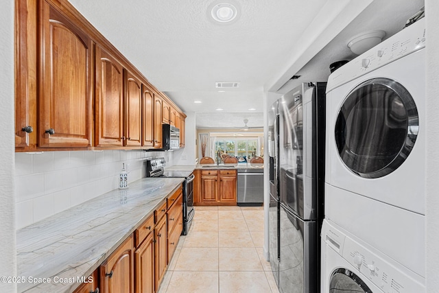 kitchen with light tile patterned floors, sink, stacked washing maching and dryer, stainless steel appliances, and tasteful backsplash