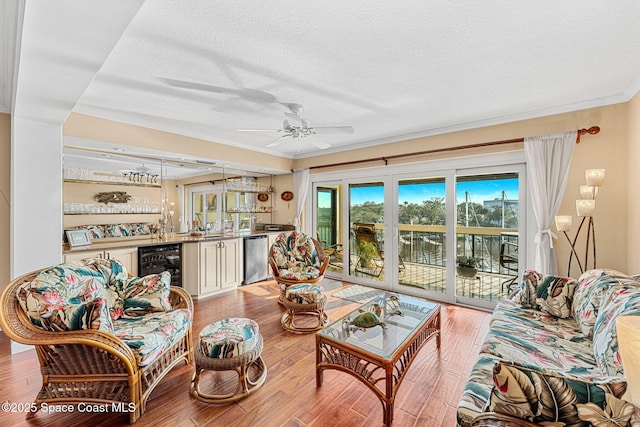 living room featuring light hardwood / wood-style flooring, ceiling fan, a textured ceiling, wet bar, and beverage cooler