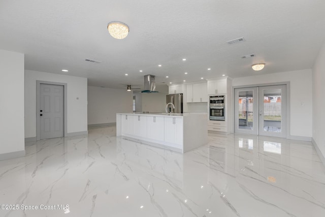 kitchen with a large island, stainless steel appliances, island range hood, white cabinets, and a textured ceiling