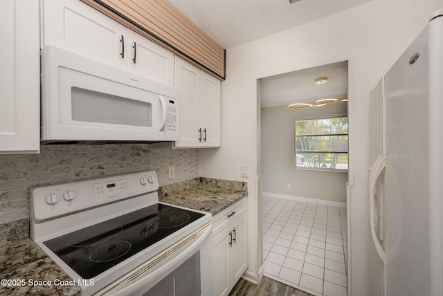 kitchen featuring white cabinetry, tasteful backsplash, dark tile patterned flooring, stone counters, and white appliances