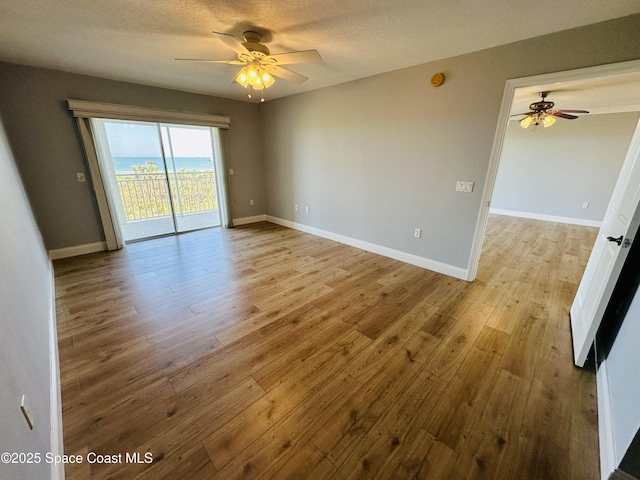 empty room with a textured ceiling, ceiling fan, and light hardwood / wood-style flooring