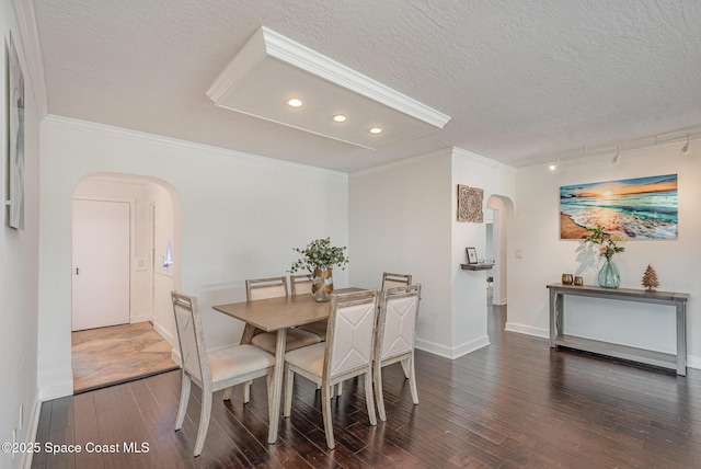 dining space with dark wood-type flooring, ornamental molding, and a textured ceiling