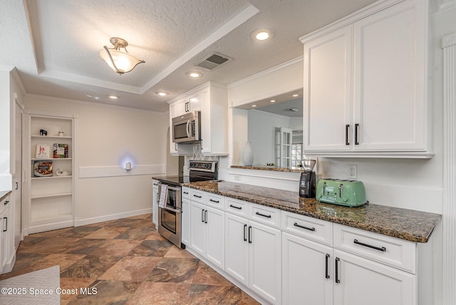 kitchen featuring a textured ceiling, dark stone countertops, appliances with stainless steel finishes, a tray ceiling, and white cabinets