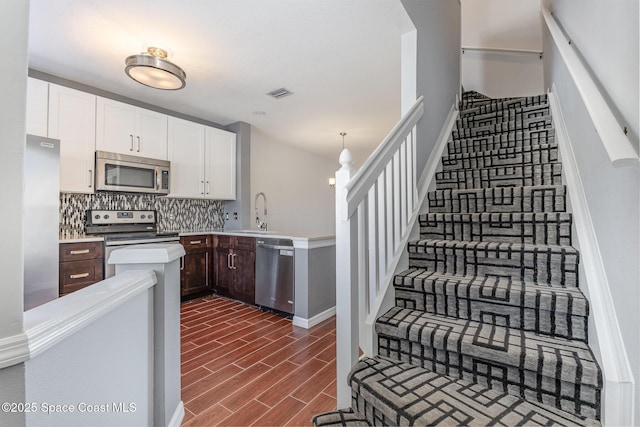 kitchen featuring dark brown cabinetry, hanging light fixtures, appliances with stainless steel finishes, white cabinets, and backsplash