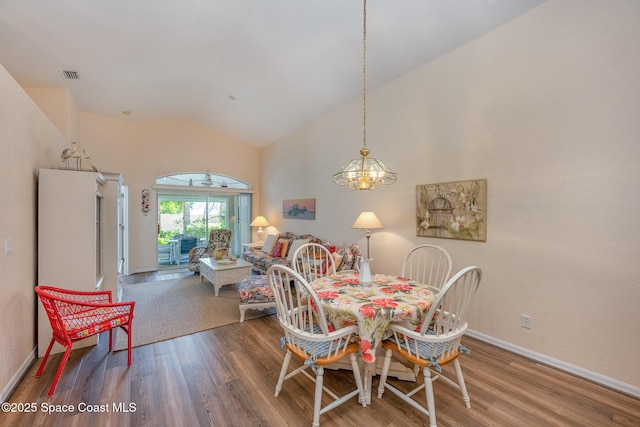 dining area with hardwood / wood-style flooring, a chandelier, and high vaulted ceiling