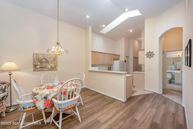 dining area featuring high vaulted ceiling, a skylight, and light hardwood / wood-style floors