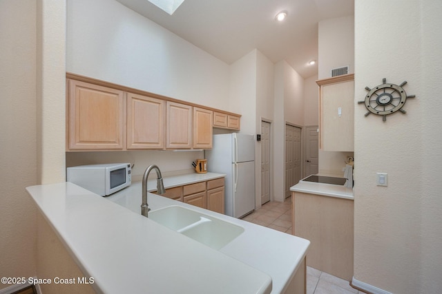 kitchen with light brown cabinetry, sink, white appliances, and kitchen peninsula