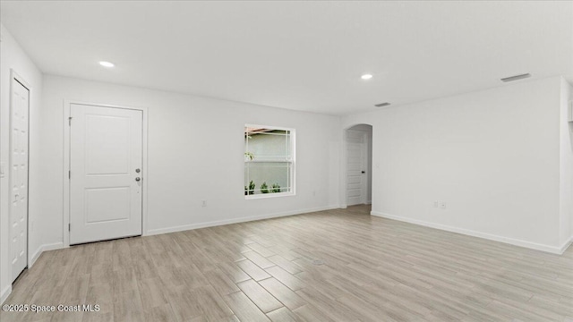 empty room featuring arched walkways, baseboards, visible vents, and light wood-style floors