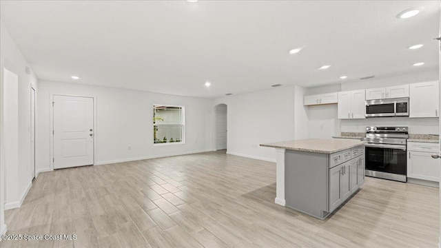 kitchen with light wood finished floors, arched walkways, a center island, stainless steel appliances, and recessed lighting