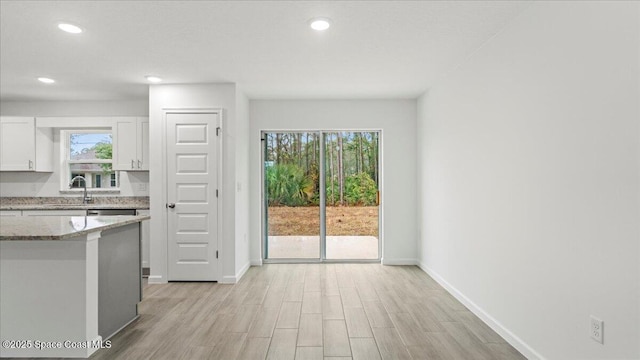 kitchen with a sink, white cabinetry, baseboards, light stone countertops, and light wood finished floors