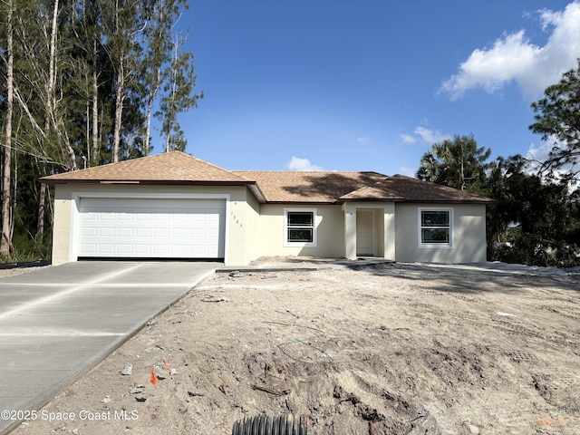 single story home featuring an attached garage, a shingled roof, concrete driveway, and stucco siding