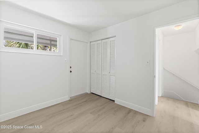 unfurnished bedroom featuring light wood-style flooring, baseboards, and a closet