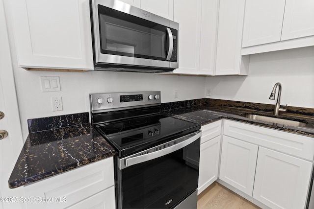 kitchen featuring light wood finished floors, stainless steel appliances, white cabinetry, a sink, and dark stone counters