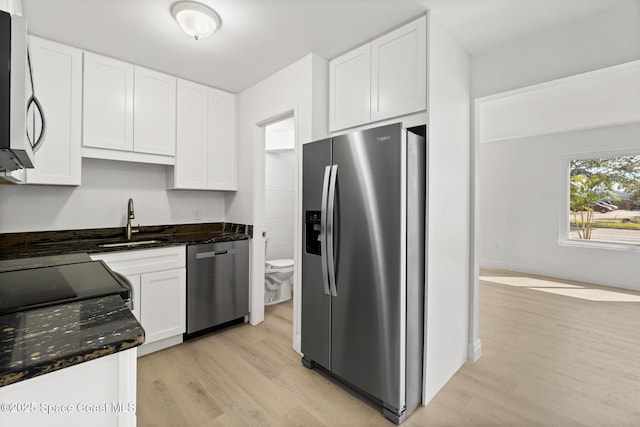 kitchen featuring sink, appliances with stainless steel finishes, light hardwood / wood-style floors, white cabinets, and dark stone counters