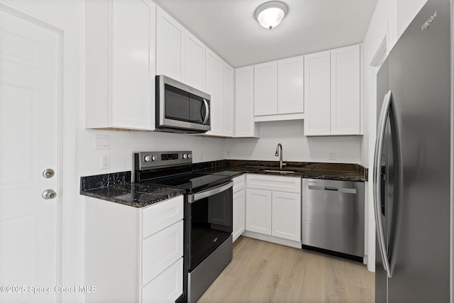 kitchen with dark stone countertops, stainless steel appliances, light wood-style floors, white cabinetry, and a sink