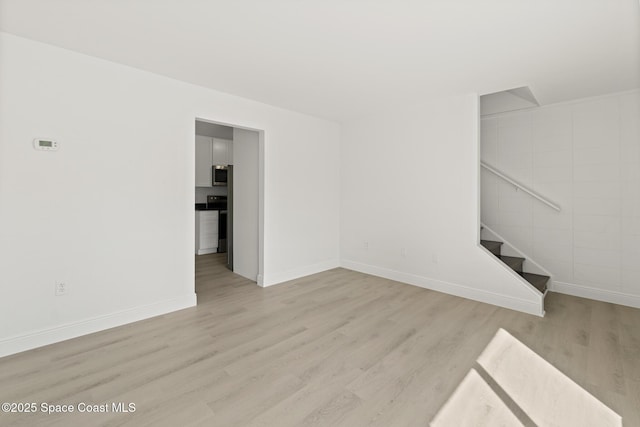 unfurnished living room featuring light wood-type flooring, baseboards, and stairway